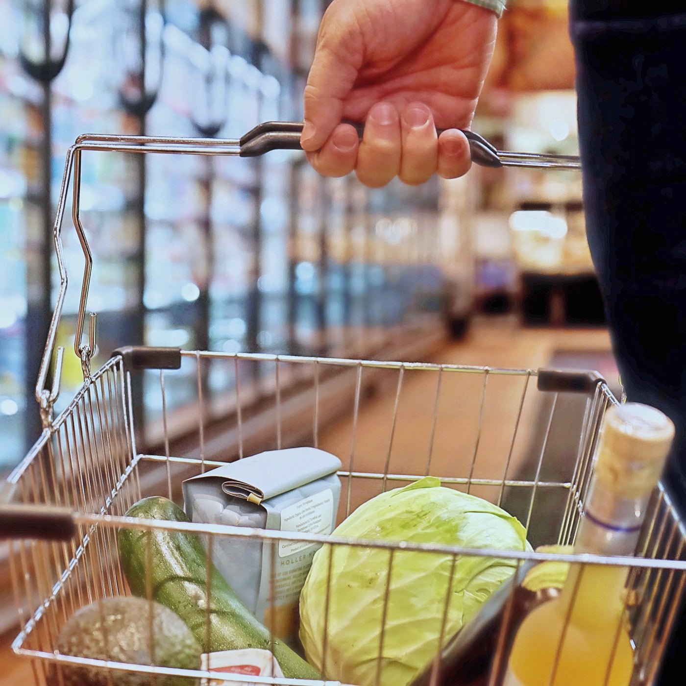 Hand holding a shopping basket with fresh vegetables