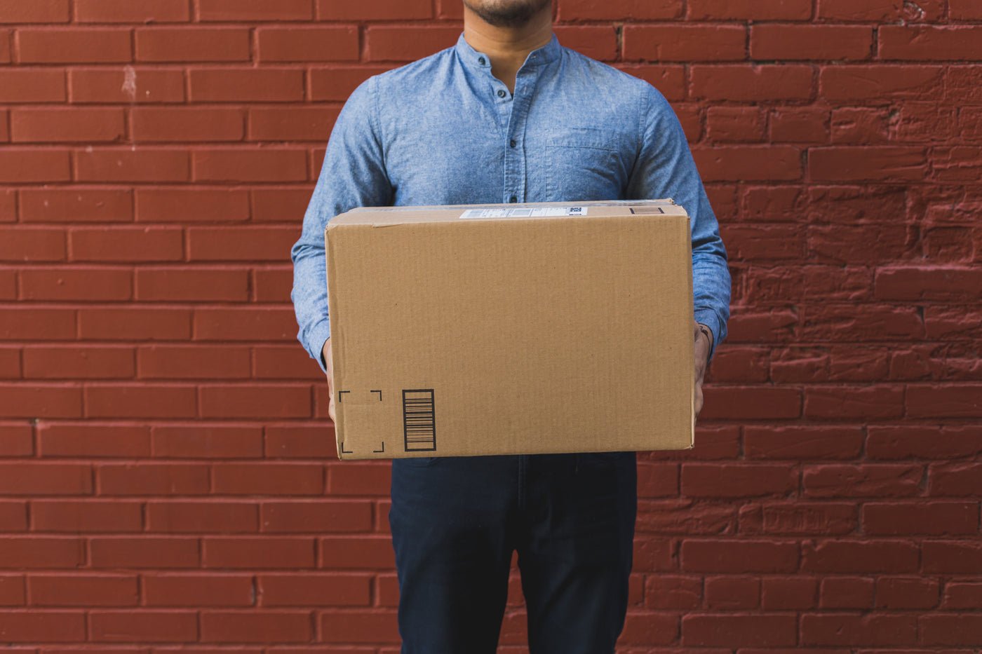 Man holding a shipping box in front of a red brick wall