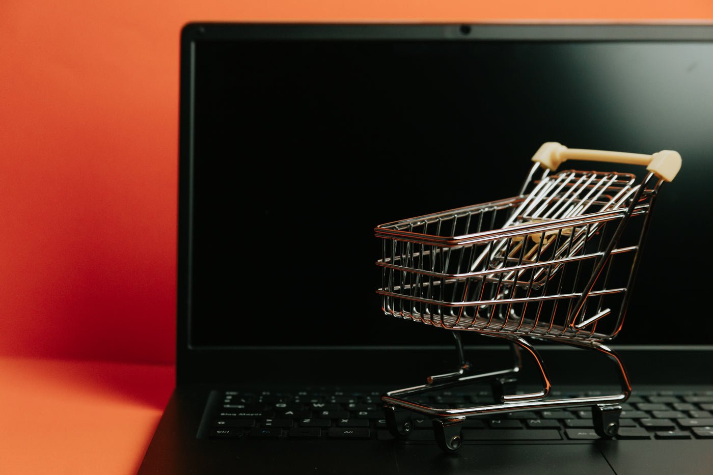 Miniature shopping cart in front of a laptop, an ecommerce concept